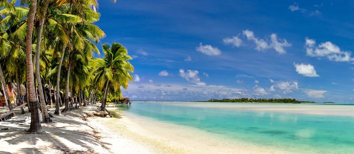 Ohromující širokoúhlý výhled na krásnou pláž na odlehlém ostrově Aitutaki severně od hlavního ostrova Rarotonga, Cookovy ostrovy. Bílá písečná pláž, mělká voda, palmy a bungalovové letovisko
